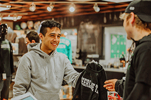 student working in store showing ctc sweatshirt to another student
