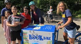 Teacher on the book bike with students and their new books standing by