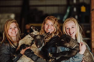 three female students pose with goats in the barn