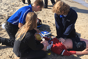 three students work on mannequin during a beach rescue