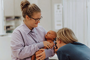 female student holding baby while another female student checks ears of baby