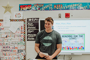 male student in front of classroom giving presentation to class